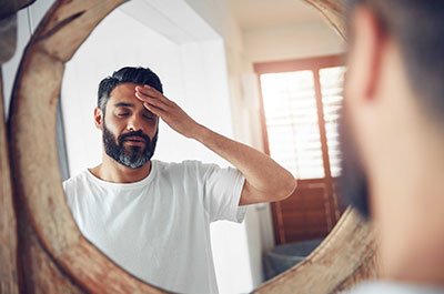 man looking in mirror rubbing forehead