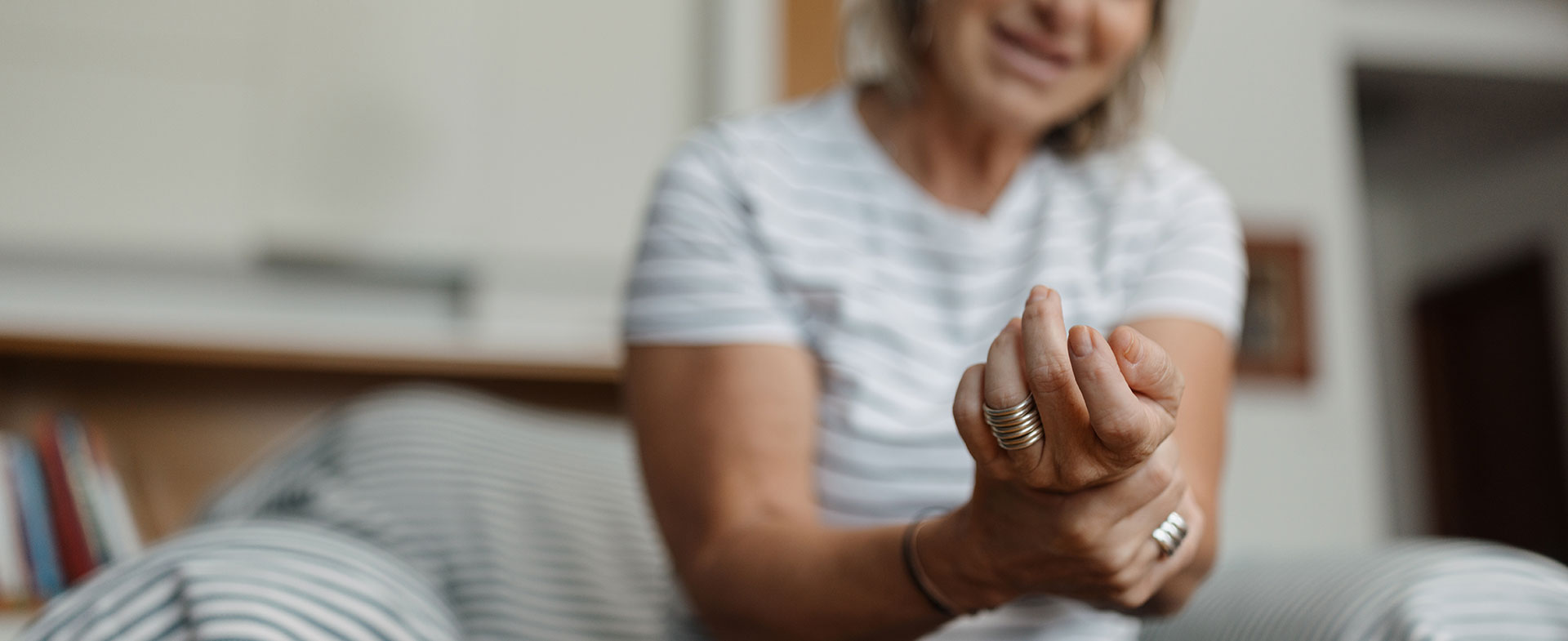 A blond woman in a striped short-sleeve shirt sits while holding her wrist in discomfort. muscle spasms after stroke