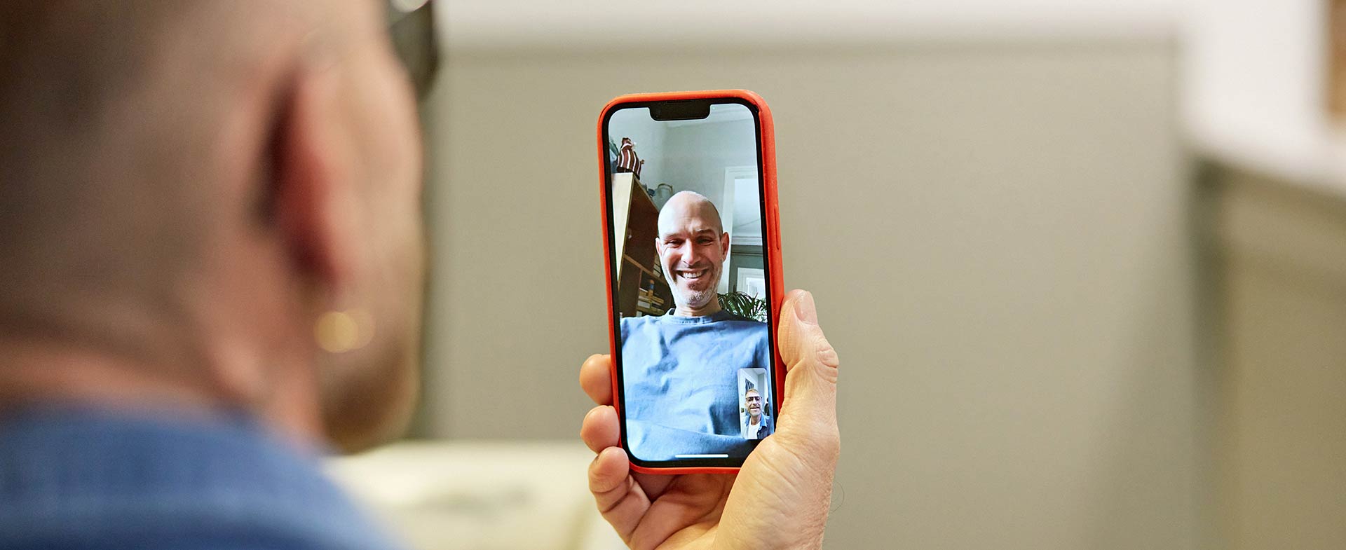 A person is using a smartphone to video call another person, whose image is visible on the screen. The person on the screen is smiling. real digital connections