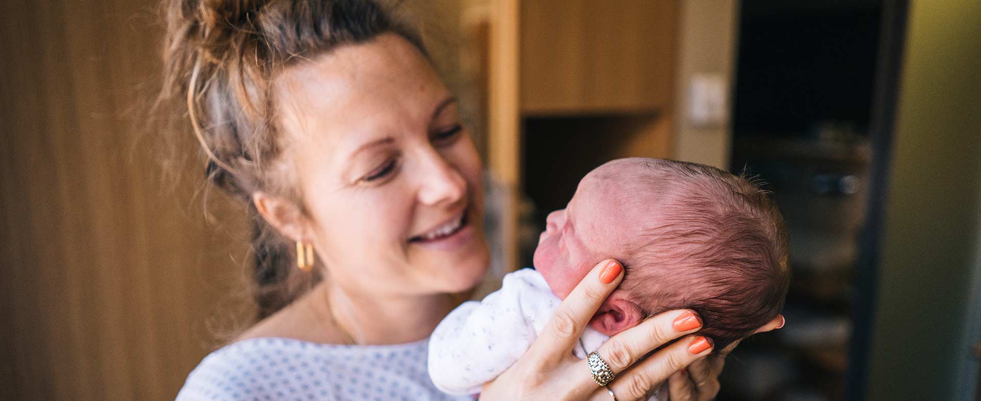 A woman in a hospital gown happily holding up her newborn baby. postpartum checklist