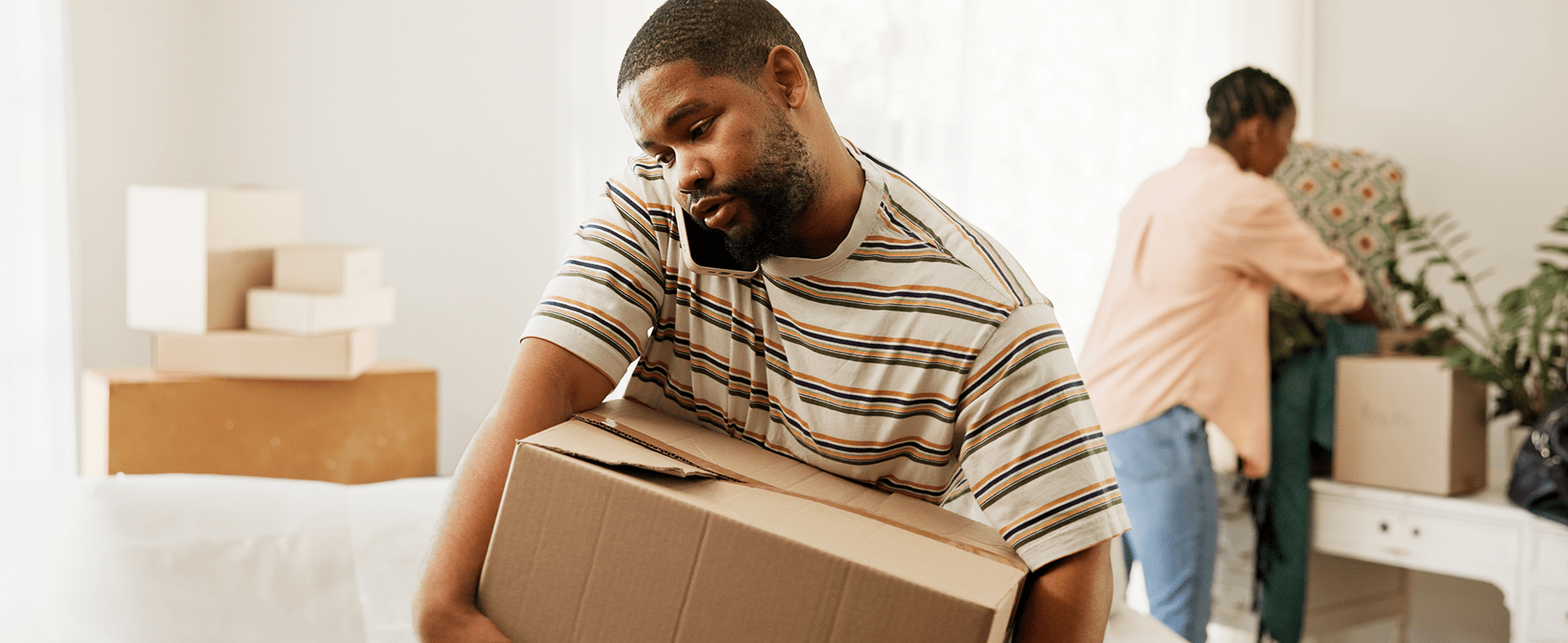 Man wearing striped t-shirt talking on the phone and carrying a box on moving day. dummy desktop Image