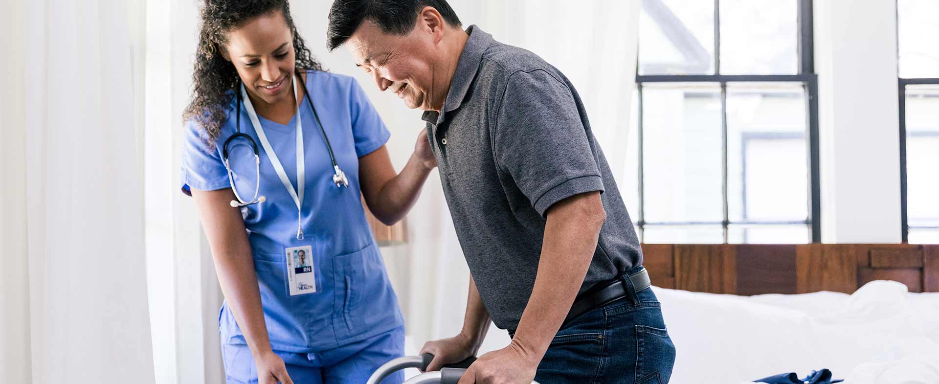A female nurse observes as a male patient stands up from bed with the help of a walker. inpatient stroke rehab