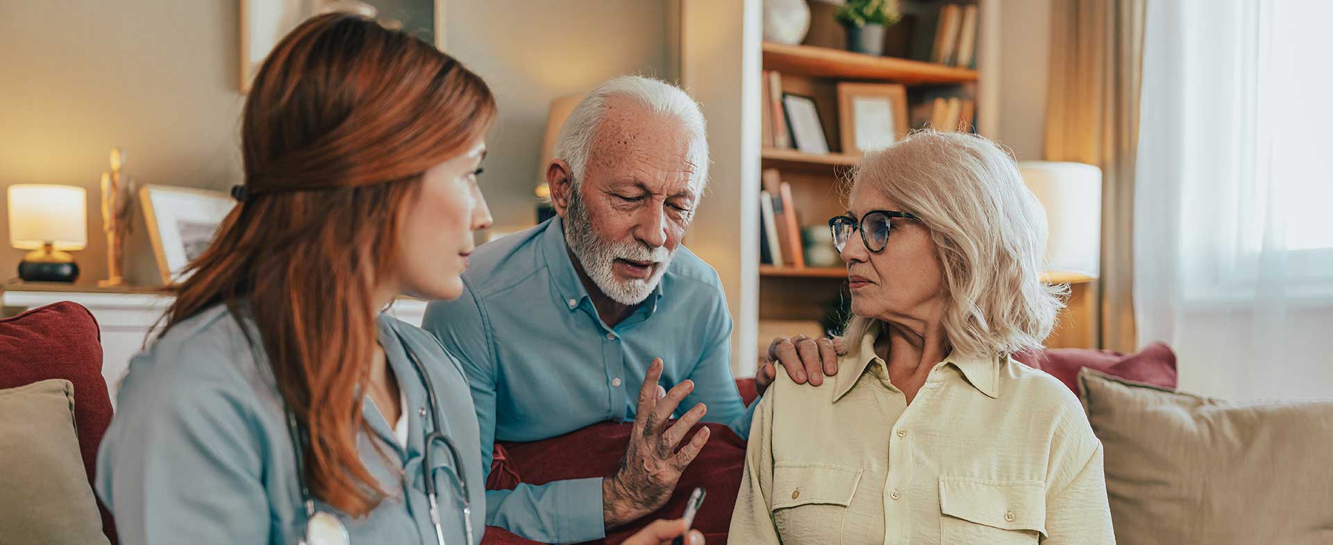 An older couple sits around a couch while talking to a female medical professional. parkinsons and delusions