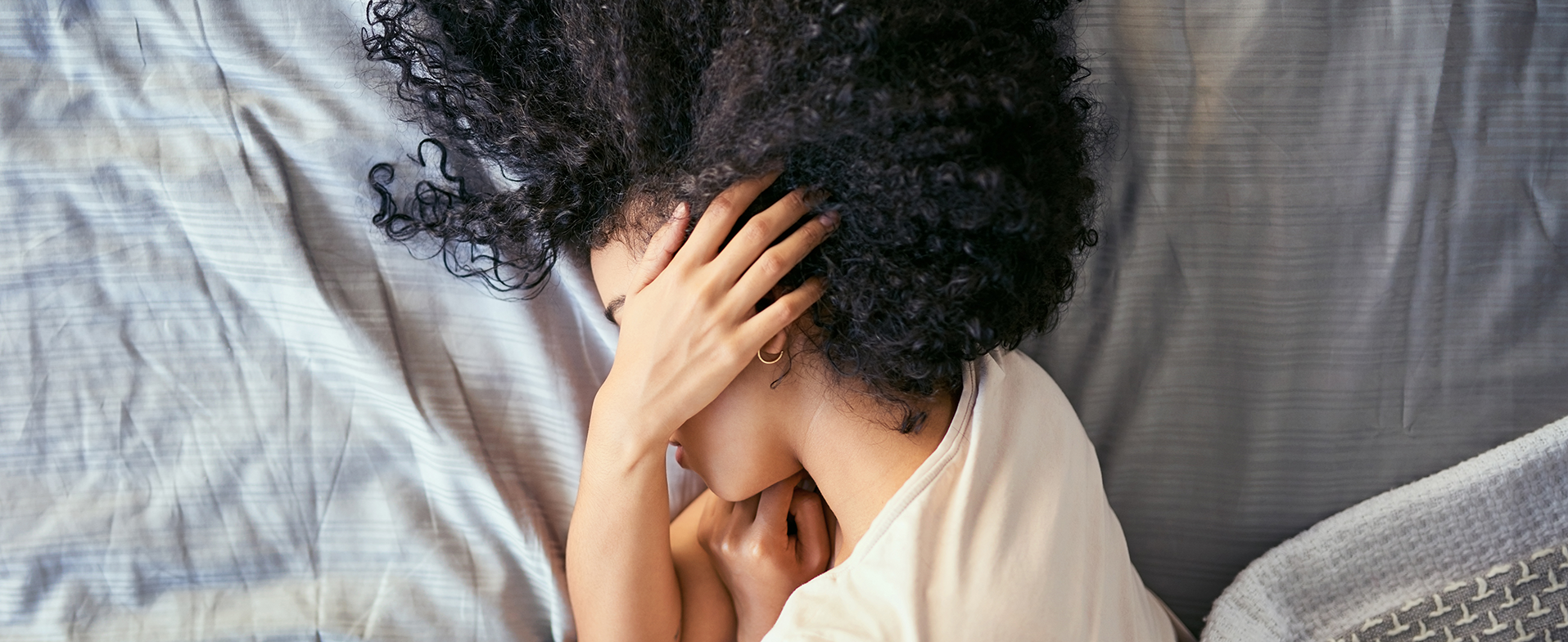 Woman with dark curly hair laying in bed with hand over her ear. dummy desktop Image