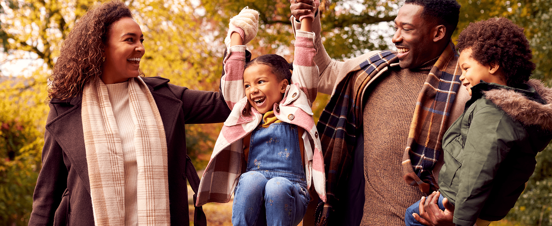 Family outside in the fall. From left to right: Mom with brown curly shoulder-length hair wearing a brown coat and white and tan plaid scarf, young daughter wearing overalls and a white and pink plaid coat, dad wearing a brown sweater and plaid scarf, and young son wearing an army green coat with a fur-lined hood. feel good hormones