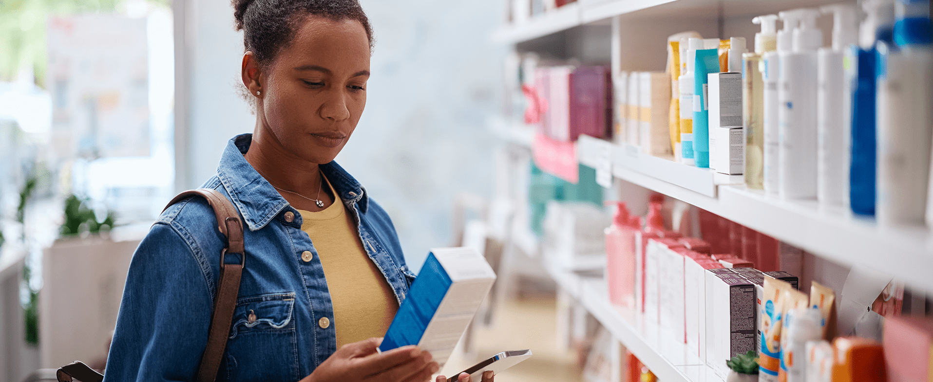 Middle-aged woman in a pharmacy looking at supplements. She has her hair in a high bun and is wearing a denim jacket with a yellow T-shirt underneath. dummy desktop Image