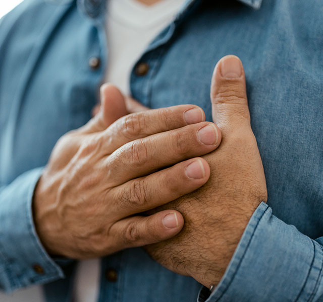 A closeup of man in a denim shirt holding both hands over his heart. coronary calcium scan