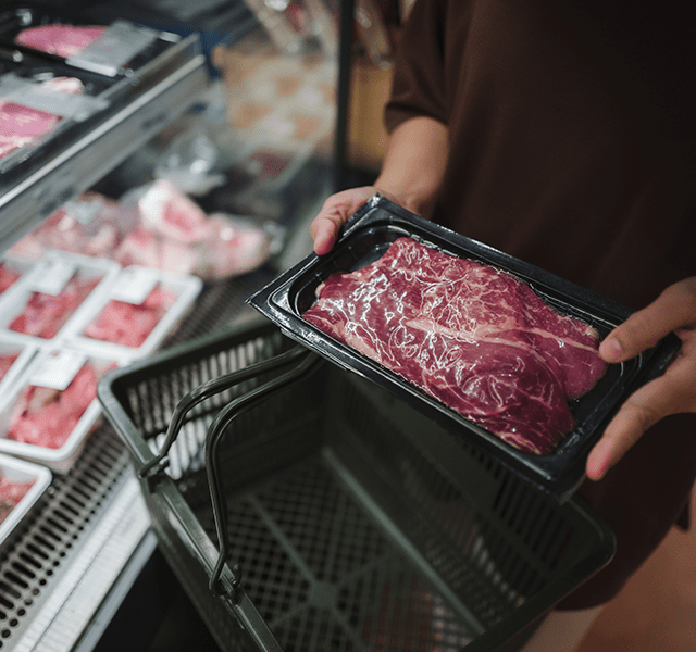 Close-up of someone putting red meat in a shopping cart at the grocery store. dummy mobile image