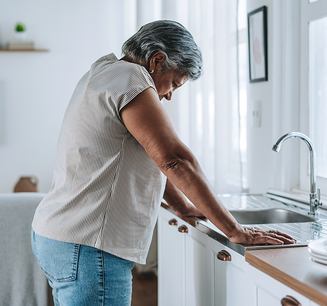 Older woman leaning over sink looking tired wearing beige T-shirt. woman with brain fog