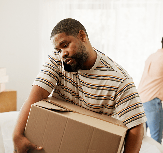 Man wearing a striped t-shirt and carrying a box while talking on the phone on moving day. dummy mobile image