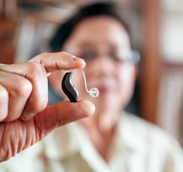 A person holds a hearing aid up close, with a blurred background. hearing health and dementia