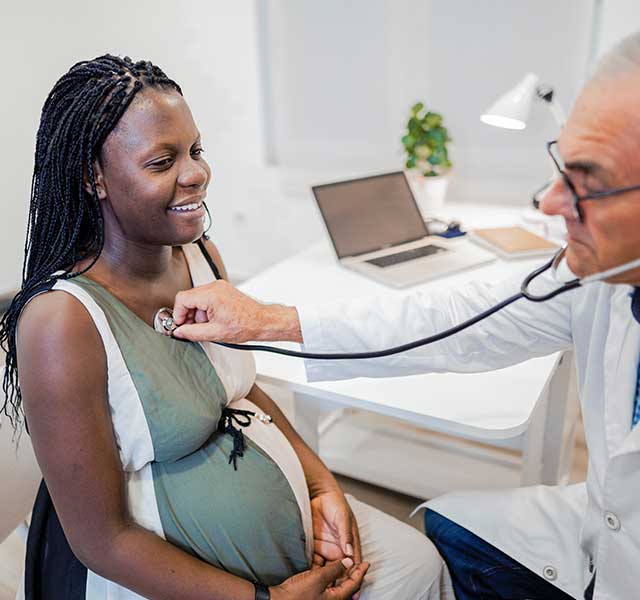 A pregnant woman sits while a male doctor uses a stethoscope to listen to her heart. pregnancy heart changes