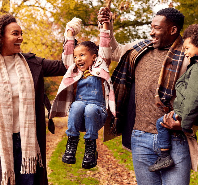 Family outside in the fall. From left to right: Mom with brown curly shoulder-length hair wearing a brown coat and white and tan plaid scarf, young daughter wearing overalls and a white and pink plaid coat, dad wearing a brown sweater and plaid scarf, and young son wearing an army green coat with a fur-lined hood. feel good hormones