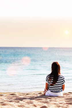 woman sitting on beach staring out into the ocean